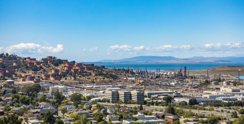 pexels-photo-12119586-12119586 Aerial view of an urban area with an oil refinery by the sea and mountains.